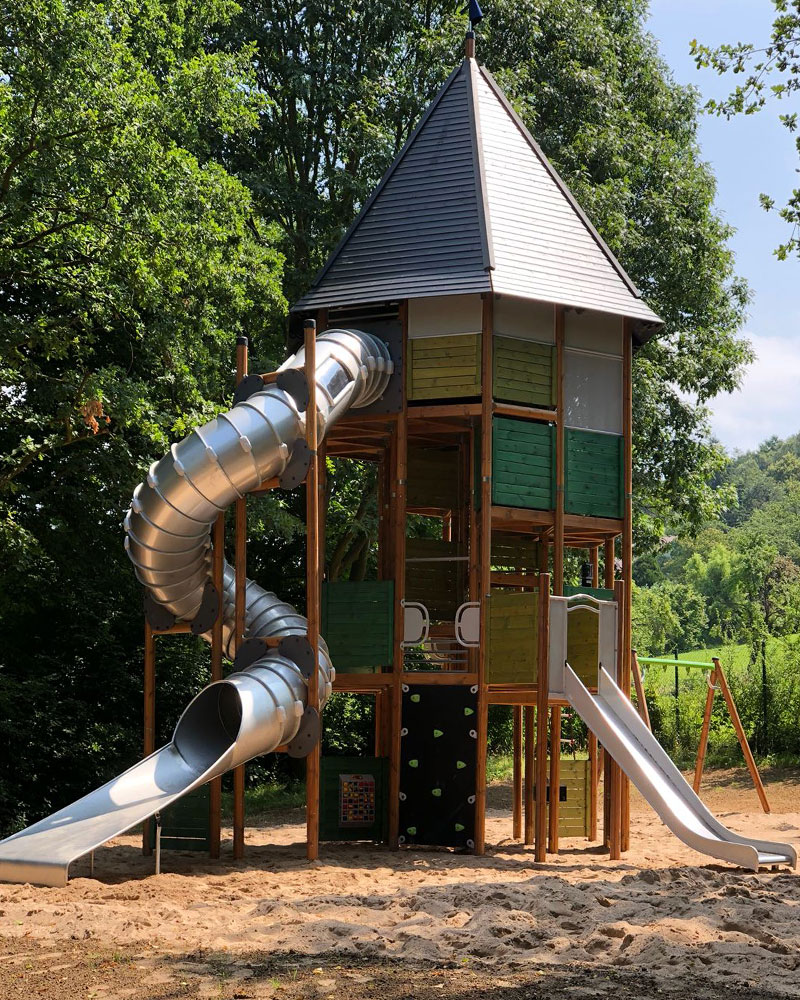 Tall wooden playground unit with a pointy triangular top, makes it looks like a mini castle.